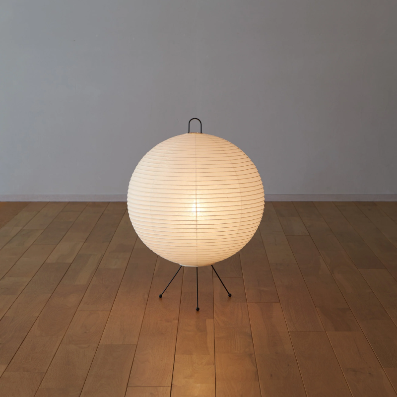 The Mari Lamp - A122 from Asano, a small rice paper table lamp turned on while on the floor of a lounge.