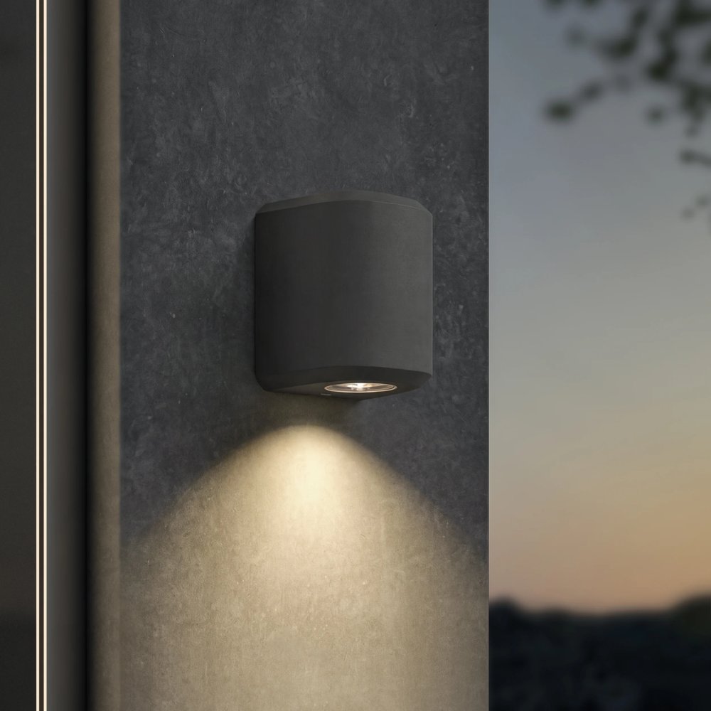 The Brixham Wall Single outdoor sconce in charcoal concrete by Astro Lighting installed on a concrete wall at night.