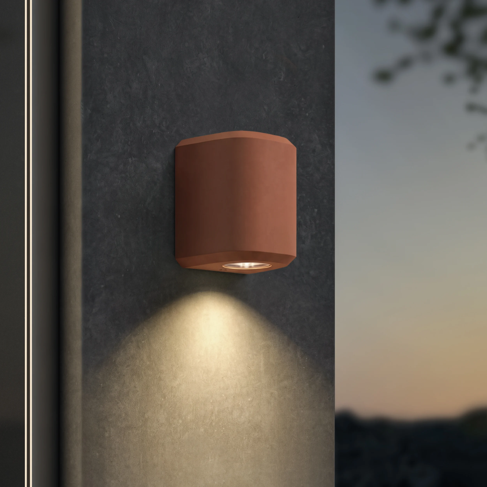 The Brixham Wall Single outdoor sconce in terracotta concrete by Astro Lighting installed on a concrete at night.