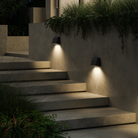 The Mast Twin Coastal Outdoor Wall Sconce by Astro Lighting in charcoal concrete installed outside on a wall in a stairway at night.