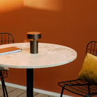 The Column Portable Table Lamp from Audo Copenhagen in anodized aluminum in an outdoor patio dining setting.
