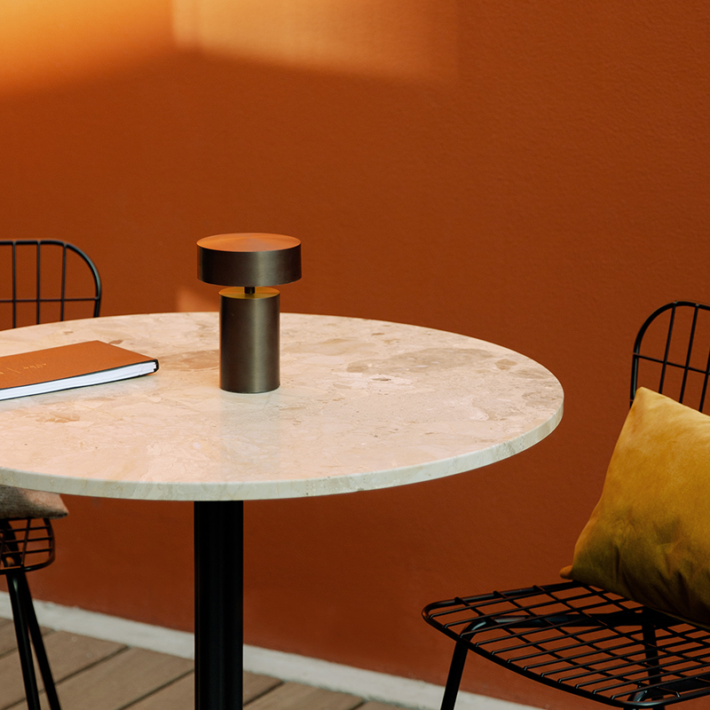 The Column Portable Table Lamp from Audo Copenhagen in anodized aluminum in an outdoor patio dining setting.
