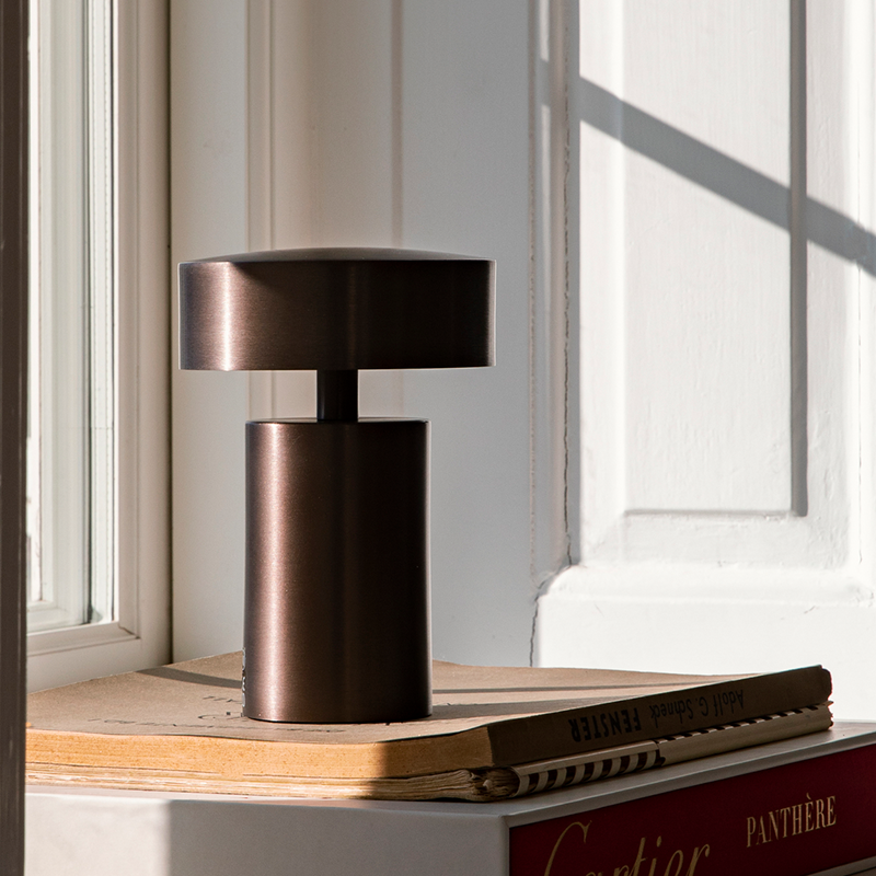 The Column Portable Table Lamp from Audo Copenhagen in anodized aluminum in a window sill.