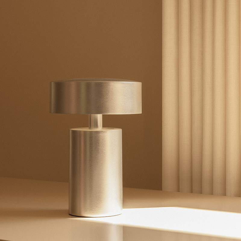 The Column Portable Table Lamp from Audo Copenhagen in brushed aluminum in a living room.