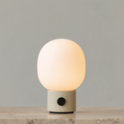 The JWDA Portable Table Lamp from Audo Copenhagen in alabaster white in a lounge with the light turned on.