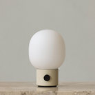 The JWDA Portable Table Lamp from Audo Copenhagen in alabaster white on a marble shelf.