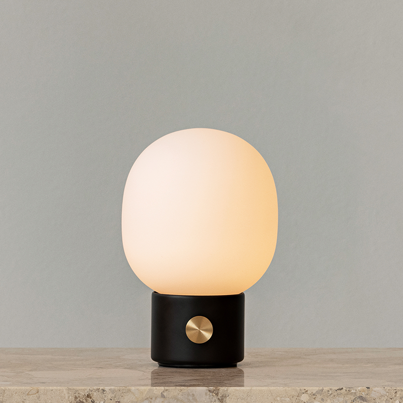 The JWDA Portable Table Lamp from Audo Copenhagen in black in a living room with the light turned on.