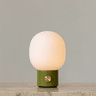 The JWDA Portable Table Lamp from Audo Copenhagen in dusty green on a marble counter.