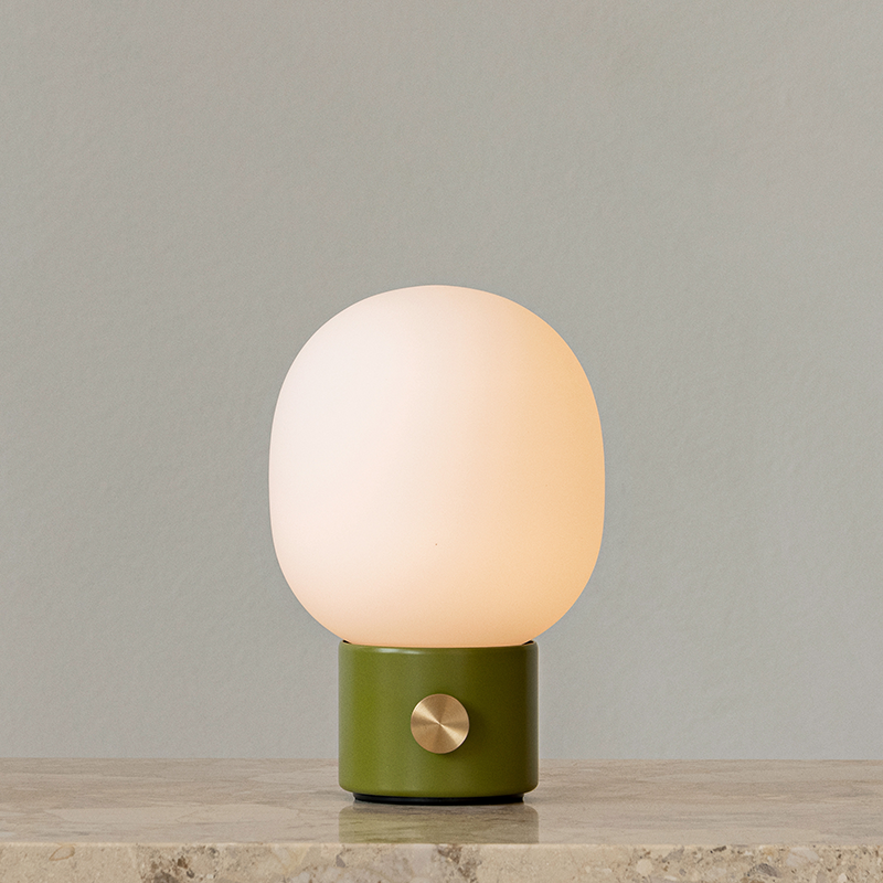 The JWDA Portable Table Lamp from Audo Copenhagen in dusty green on a marble counter.