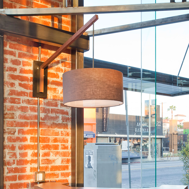 The Talea Wall Sconce Swing Arm from Cerno in Burlap with brushed aluminum and walnut in a storefront.
