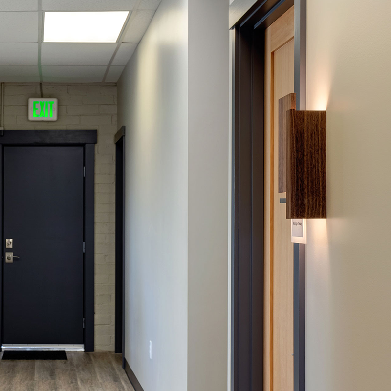 The Vesper Wall Sconce from Cerno in oiled walnut in a hotel hallway.