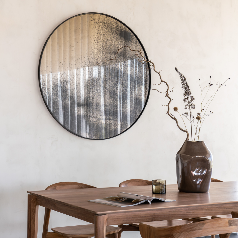 The Aged Wall Mirror Round 36 inch in Bronze by Ethnicraft in a dining room.