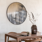 The Aged Wall Mirror Round 36 inch in Bronze by Ethnicraft in a dining room.
