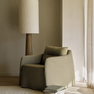 The Weave Lounge Chair by Ethnicraft in green, with a stack of books next to a tall floor lamp in a softly lit room.