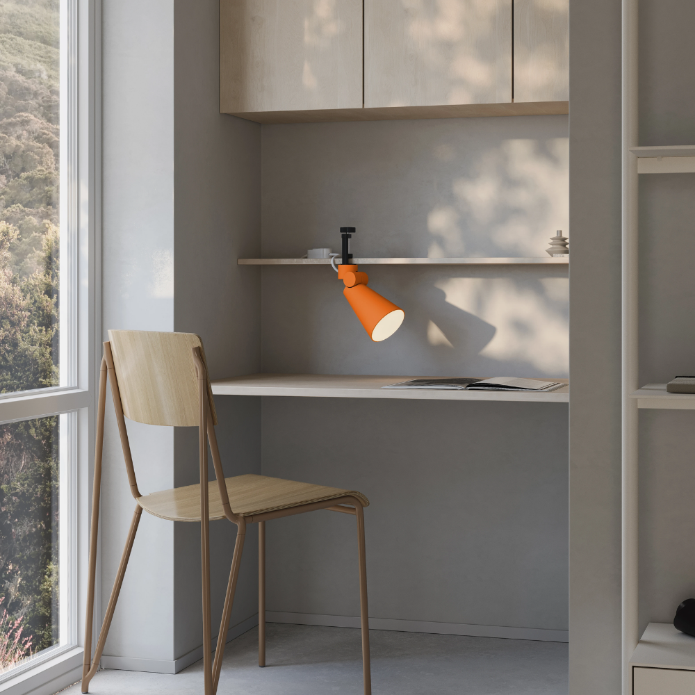The persimmon Aim Clamp Light from Gantri with the black clamp in a home office.