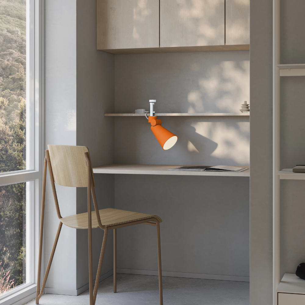 The persimmon Aim Clamp Light from Gantri with the white clamp in a living room.