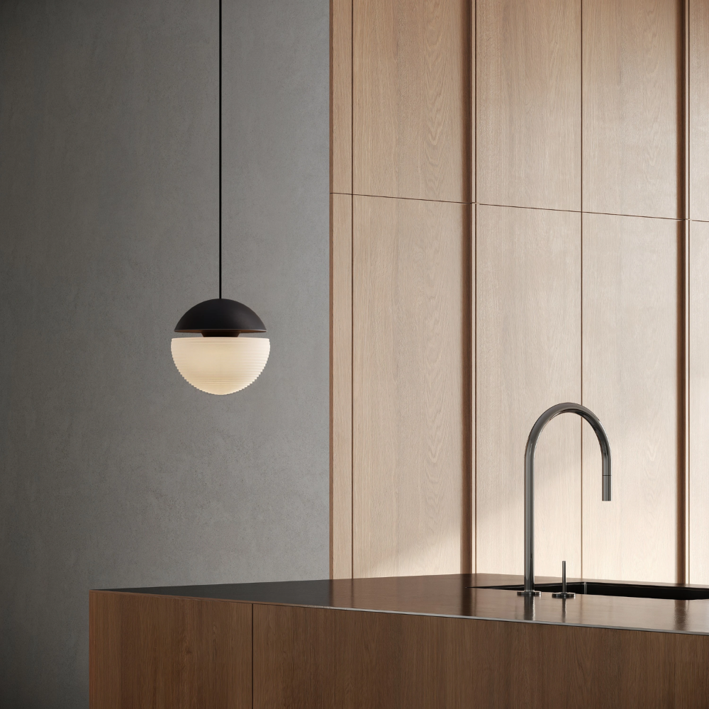 The carbon Cora Pendant Light from Gantri with the black cord in a kitchen and dining area above an island with a sink.