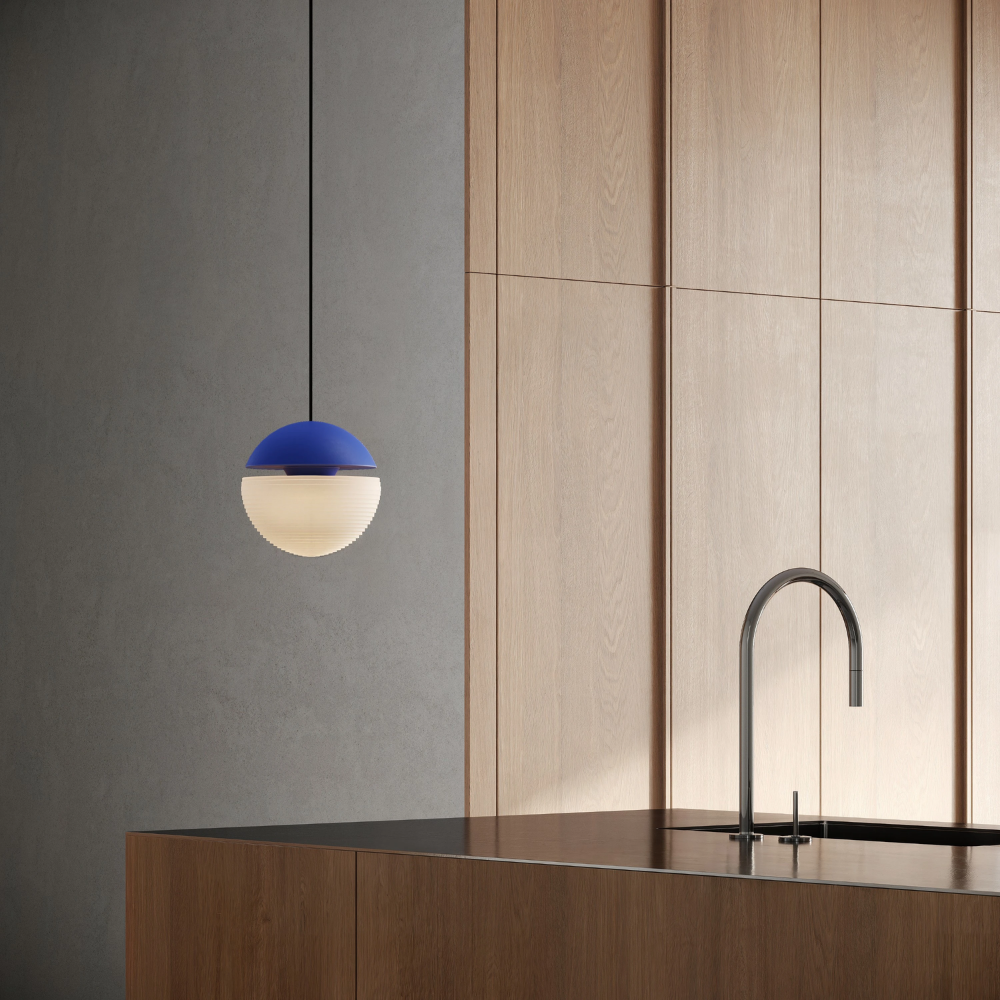 The cobalt Cora Pendant Light from Gantri with the black cord in a kitchen and dining area above an island with a sink.