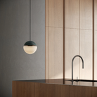 The forest Cora Pendant Light from Gantri with the black cord in a kitchen and dining area above an island with a sink.