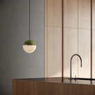 The olive Cora Pendant Light from Gantri with the black cord in a kitchen and dining area above an island with a sink.