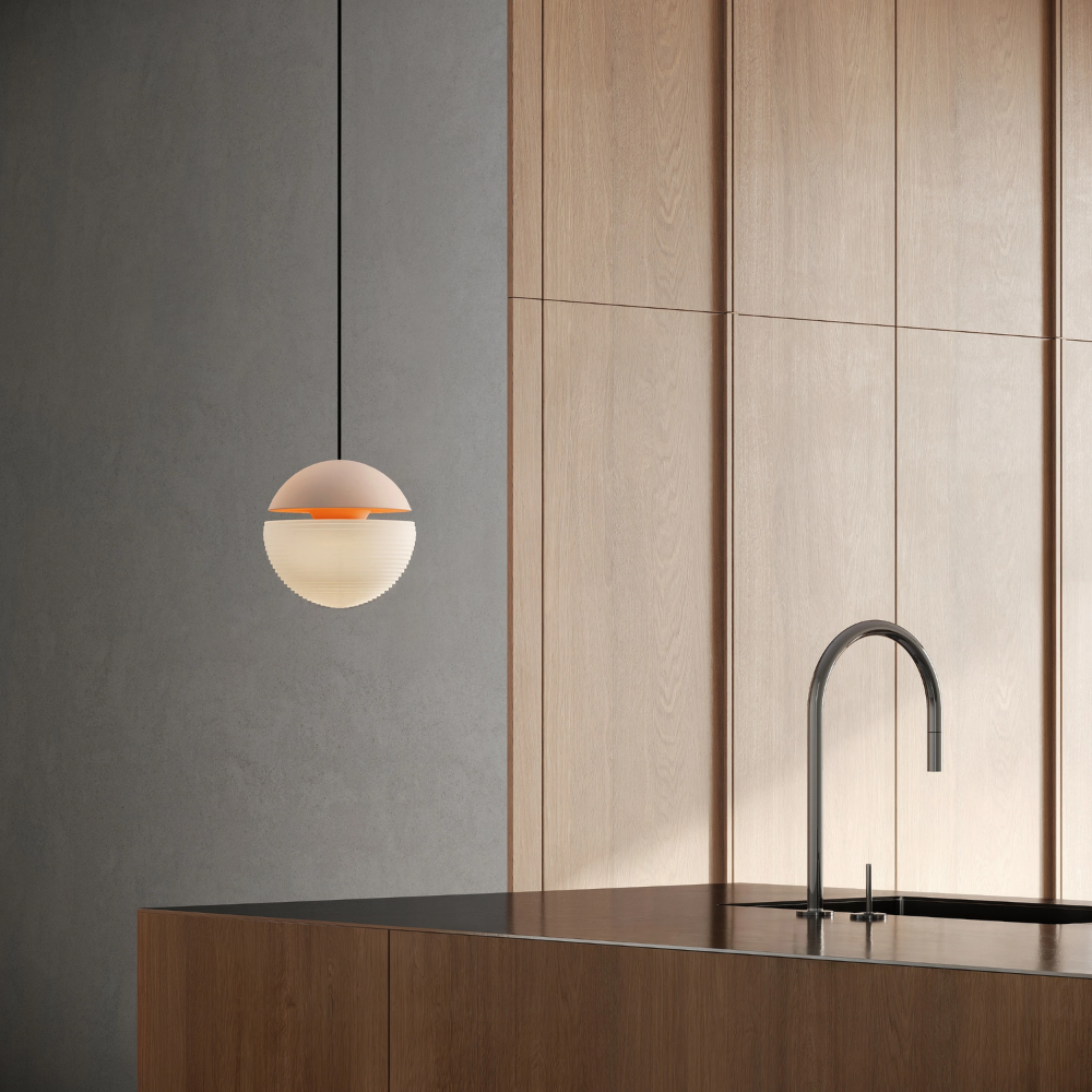 The peach Cora Pendant Light from Gantri with the black cord in a kitchen and dining area above an island with a sink.