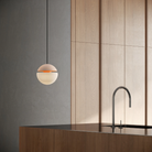 The peach Cora Pendant Light from Gantri with the black cord in a kitchen and dining area above an island with a sink.