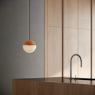 The persimmon Cora Pendant Light from Gantri with the black cord in a kitchen and dining area above an island with a sink.