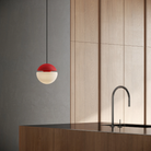 The poppy Cora Pendant Light from Gantri with the black cord in a kitchen and dining area above an island with a sink.