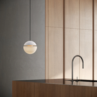 The snow Cora Pendant Light from Gantri with the black cord in a kitchen and dining area above an island with a sink.