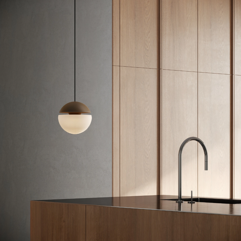 The walnut Cora Pendant Light from Gantri with the black cord in a kitchen and dining area above an island with a sink.