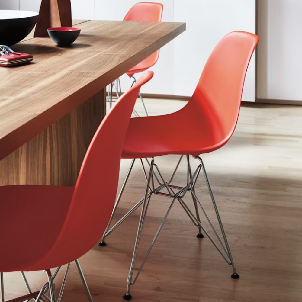 The red orange shell Eames Molded Plastic Side Chair Wire Base from Herman Miller in a dining room.