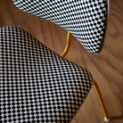 The Upholstered Eames Molded Plastic Dining Chair from Herman Miller with black and white checker upholstery, white shell and marigold leg finish close up in a dining room.