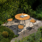 The Circle Outdoor Dining Table by Houe in the garden with chairs is surrounded by greenery.