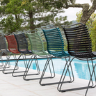 The Click Outdoor Dining Chair No Armrest by Houe is shown with multiple color options beside a pool.