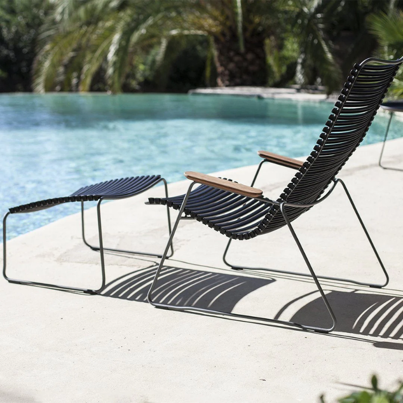 The Click Outdoor Footrest by Houe with a lounge chair beside the pool with palm trees.