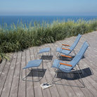 The black Click Outdoor Lounge Chair by Houe on a wooden deck with ocean view.