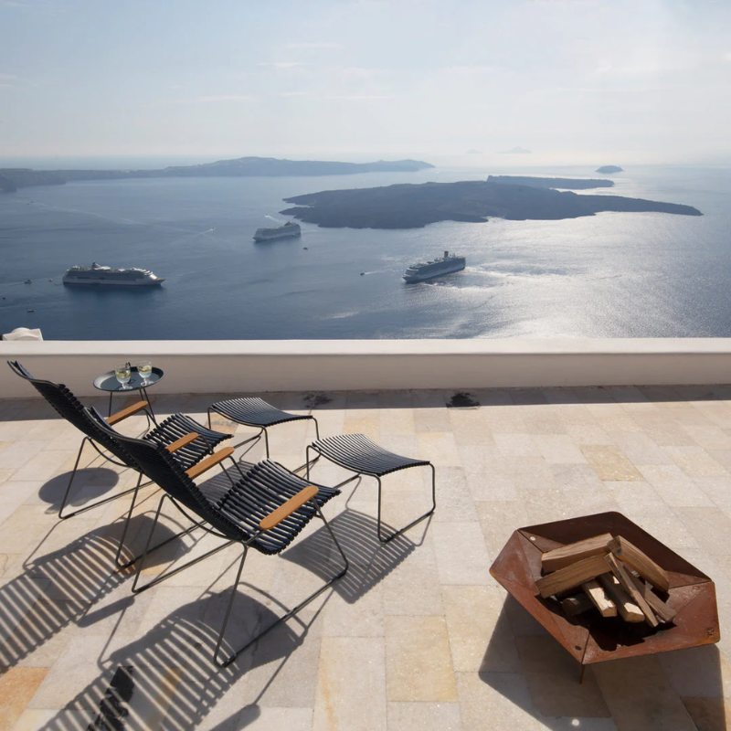 The Click Outdoor Lounge Chair by Houe with a patio and fire pit overlooking a body of water with islands and ships.