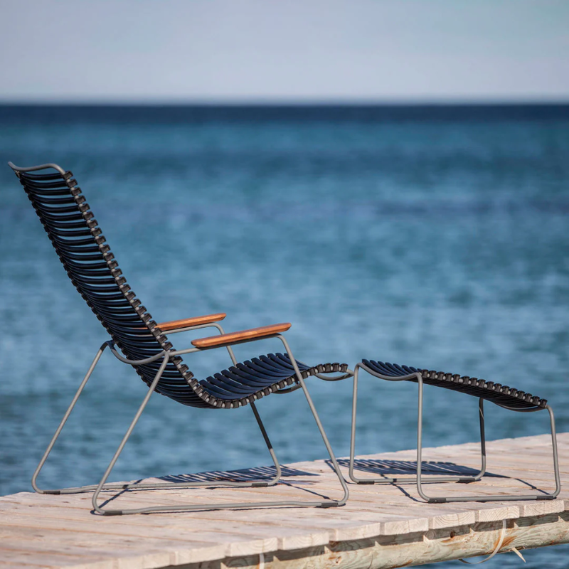 The Click Outdoor Lounge Chair by Houe with an ottoman on a wooden platform with an ocean view.