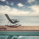 The Click Outdoor Rocking Chair by Houe on a wooden dock with a sea view.