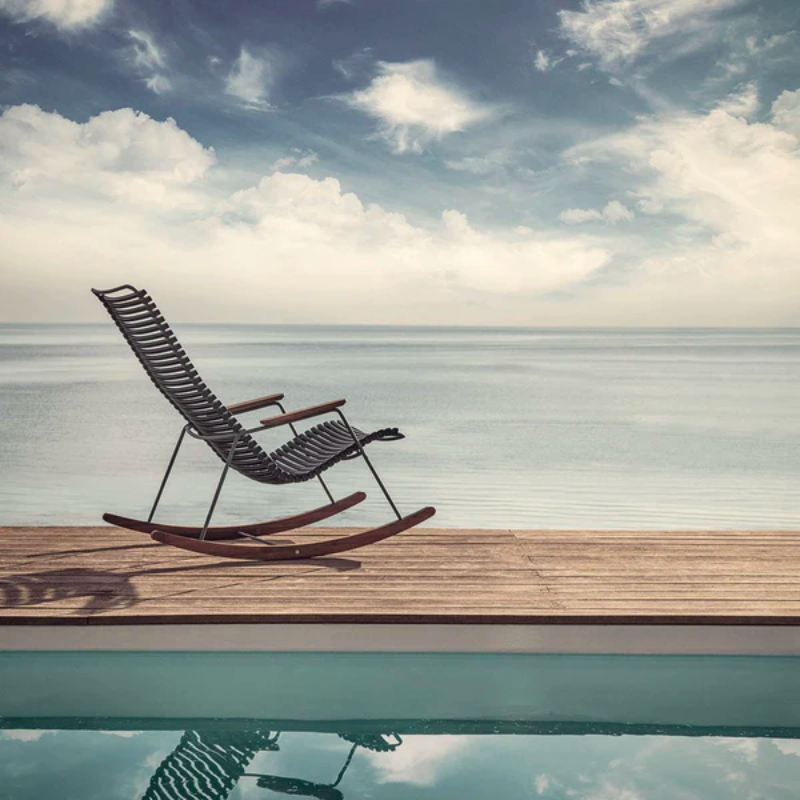 The Click Outdoor Rocking Chair by Houe on a wooden dock with a sea view.