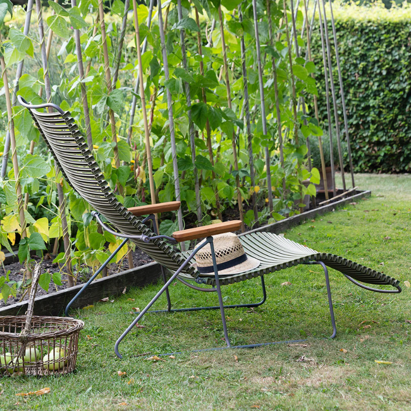 The Click Outdoor Sunlounger from Houe with a hat on a grassy area with garden plants.