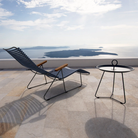 The Click Outdoor Sunlounger from Houe with a table and a scenic view of water and sky.