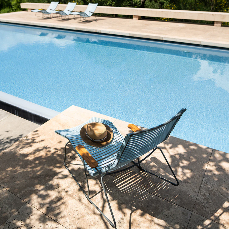 The Click Outdoor Sunrocker by Houe with a hat beside a pool.