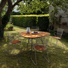 The Leaf Outdoor Dining Table by Houe in a garden setting with metal chairs on a grassy area.
