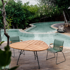 The Leaf Outdoor Dining Table by Houe with green chairs on a wooden deck from the poolside.