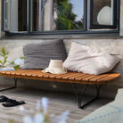 The Molo Sunbed by Houe with cushions and a hat on a patio area with a window in the background.