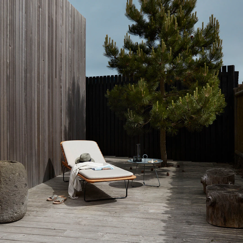 The Molo Sunbed Cushion by Houe with a table and tree outside of the house.
