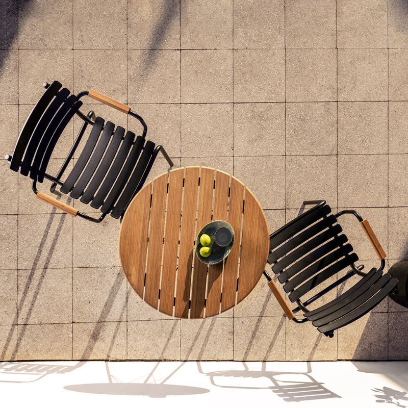 The black ReClips Outdoor Dining Chair Bamboo by Houe with a round wooden table on a tiled patio from a top view.
