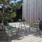 The olive green ReClips Outdoor Dining Chair Bamboo by Houe with a black table on a wooden deck.