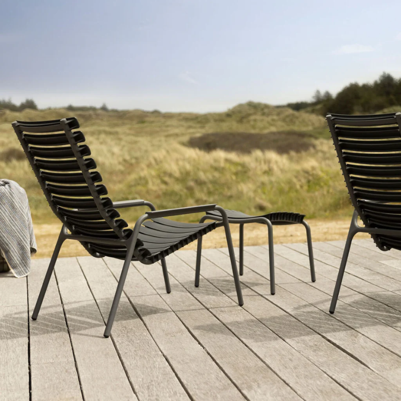 The ReClips Outdoor Lounge Chair by Houe on a wooden deck with a grassy field.